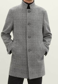 Płaszcz w czarno-białą kratę z wysokim kołnierzem, zapinany na guziki z przodu, z bocznymi kieszeniami. Wykonany z teksturowanej tkaniny.