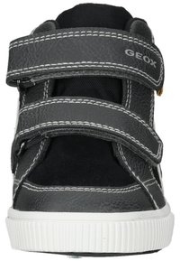 Zapatillas negras y grises con correas de Velcro, cuero texturizado y tela suave, suela de goma blanca y detalles de costura blanca visibles.