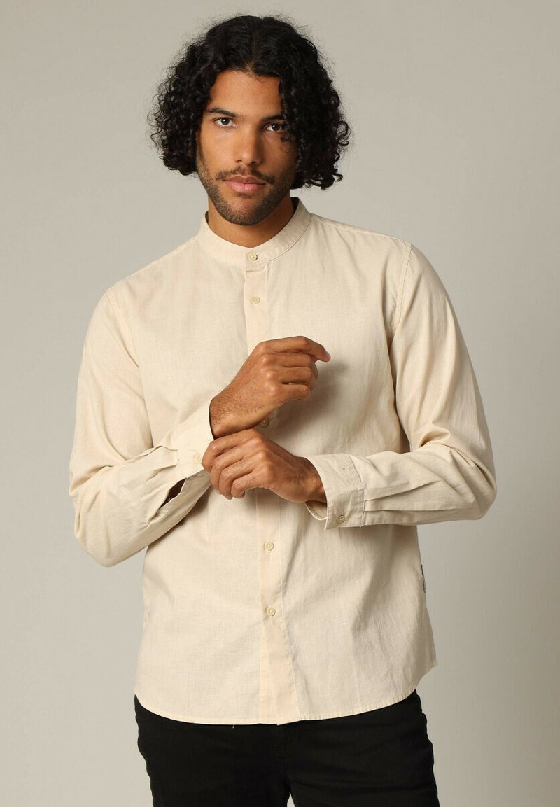 Lichtbeige overhemd met knopen zonder kraag, lange mouwen en een subtiele textuur. Voorzien van kleine knopen en een ontspannen pasvorm.