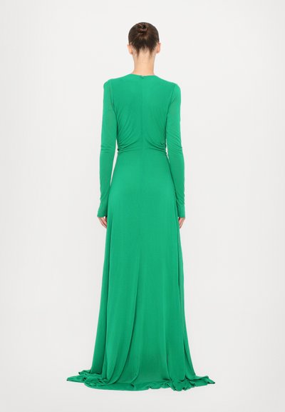 Rochie verde cu mâneci lungi, realizată dintr-un material neted, elastic; are un spate pliat și o fustă până la podea. Accesorii minime.