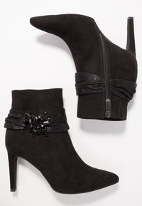 Botas de tobillo de ante negro con punta afilada y un alto tacón de aguja. Presentan una banda decorativa negra con un detalle de cuentas y cierre de cremallera.