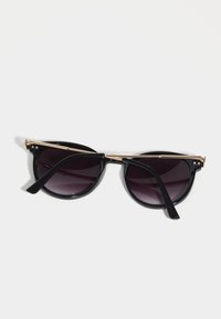 Black sunglasses with a cat-eye shape, gradient dark lenses, gold accents on the bridge and temples, and glossy black frames.