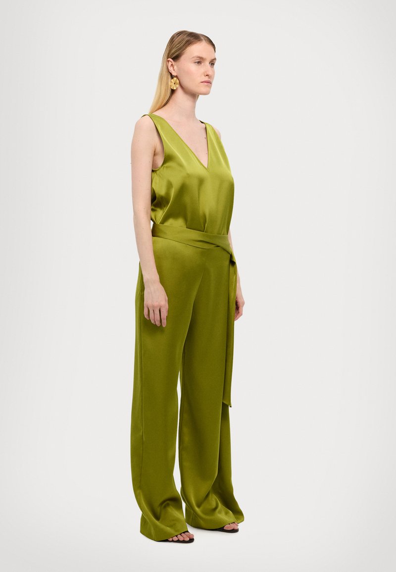 Grønn sateng jumpsuit med dyp V-hals, brede ben og belte i midjen. Glatt tekstur og minimalistisk design.