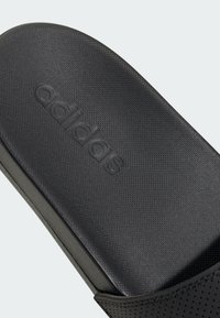 Ciabatta Adidas nera con tomaia testurizzata, caratterizzata da un logo impresso e una fascia traforata. Plantare liscio e profilo strutturato.