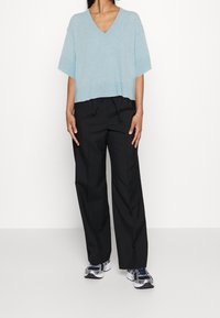 Vaaleansininen, lyhythihainen V-kaula-aukollinen neule yhdistettynä väljälahkeisiin mustiin housuihin ja sinisiin urheilukenkiin, muodostaen rento ja mukava tyyli.