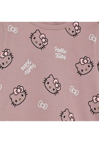 Hellrosa Stoff mit wiederholtem Hello Kitty-Gesichtsdruck, der schwarze Umrisse, pinke Schleifen und weißen Text "Hello Kitty" in verschiedenen Ausrichtungen zeigt.