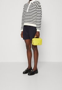 Pasiasty sweter z kołnierzykiem, granatowe szorty, czarne mokasyny oraz żółta torebka. Materiały: bawełna, skóra. Cechy wyróżniające: logo i zamki.