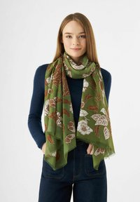 Écharpe florale verte avec une texture légère, présentant des motifs floraux marron et blanc, portée lâchement autour du cou, sur un haut bleu.