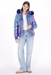 Puchowa kurtka o iryzujących odcieniach niebieskiego i fioletu z niebieskim futerkiem na kapturze, wyposażona w zamek błyskawiczny i elastyczne mankiety.