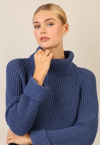 Blauer, gerippter Pullover mit hohem Kragen und langen Ärmeln. Dicke Textur mit lockerer Passform, ausgestattet mit umgeschlagenen Bündchen und modernem Design.