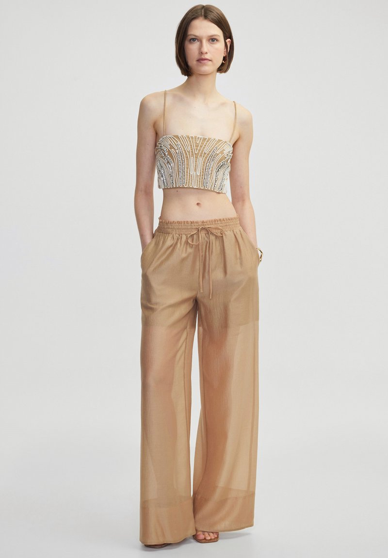 Korte bewerkte top met dunne bandjes; gecombineerd met lichte, doorzichtige beige wijde broek met elastische tailleband en zijzakken.