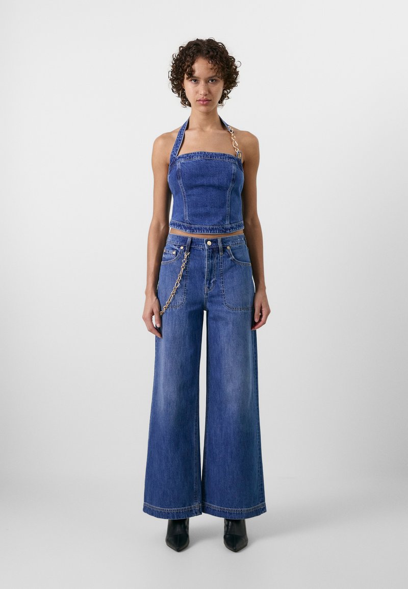 Denim halterneck top med en tætsiddende bodice og cropped længde, parret med brede denim jeans; har en kædeaccent på jeansene.