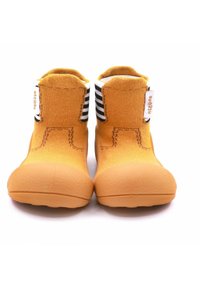 Botines de tela amarillos con una suela texturizada, acentos a rayas en blanco y negro en la parte superior y una etiqueta en el costado. Diseño suave y flexible para mayor comodidad.