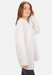 White button-up shirt with textured fabric, long sleeves, and a collar. Features front buttons and a relaxed fit. Suitable for layering.