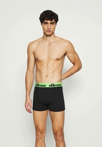 Sorte boxer briefs med en neongrønn "ellesse" merket midjebånd. Glatt tekstur, tettsittende design, midt på låret lengde, fremhever atletisk silhuett.