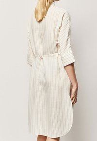 Sukienka w paski w kolorze kremowym z beżowymi liniami, z paskiem w talii i rękawami 3/4. Miękka tkanina o luźnym kroju.