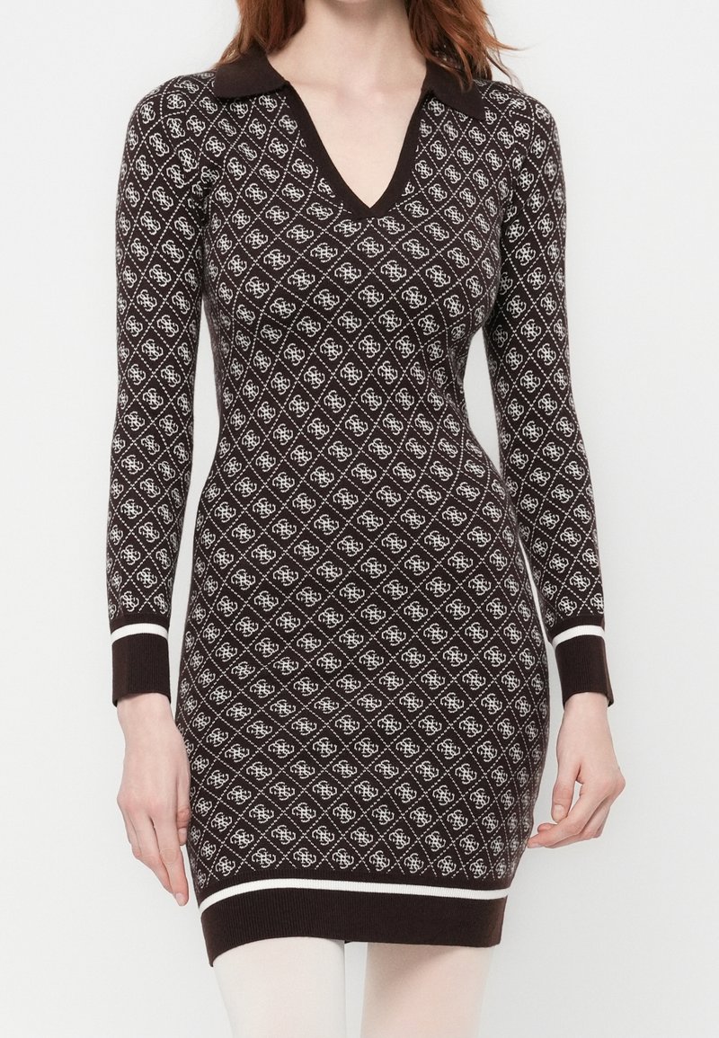 Femme portant une robe en tricot ajustée à manches longues avec un motif losanges marron et blanc et un col marron sur fond blanc.