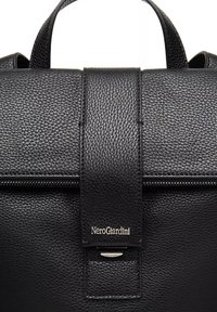 Zaino in pelle nera con finitura strutturata, dotato di chiusura a patta e dettaglio in metallo argentato. Logo impresso sulla cinghia frontale.