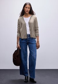 Cardigan in maglia beige con scollo a V, chiusura a bottoni e polsini a costine. Abbinato a denim blu chiaro a gamba larga e stivaletti neri.