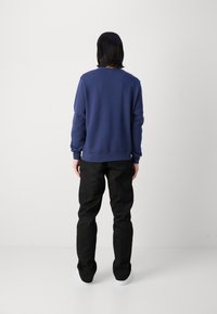 Sudadera azul marino de manga larga, corte relajado, con puños y dobladillo de punto; combinada con pantalones negros y zapatillas blancas. Diseño minimalista.
