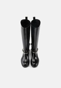 Botas de montaria em couro preto com acabamento brilhante, apresentando uma fivela de metal e alças na parte superior para fácil colocação.
