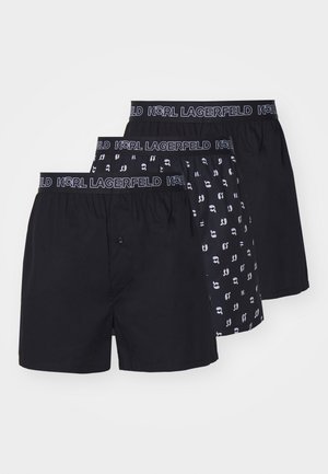 Trois paires de boxers noirs avec des ceintures élastiques. Une paire est complètement noire, les autres ont un design à motifs avec de petits graphiques.