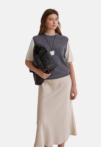 Suéter corto de manga corta gris y crema, falda midi beige, sostenido un bolso de cuero negro. Collar con un colgante floral, texturas suaves y diseño sencillo.