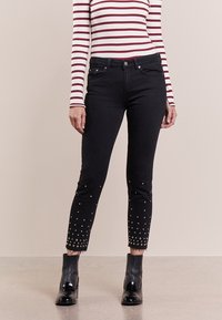 Svarta smala jeans med fransar i nederkant, dekorerade med silvernitar runt fållen. Bärs med en randig långärmad topp och ankelstövlar.