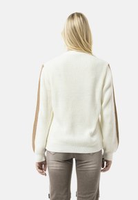 Crème gebreide trui met textuur ribbels, met contrasterende bruine accenten op de schouders. Lange mouwen, standaard pasvorm, eenvoudig ontwerp.