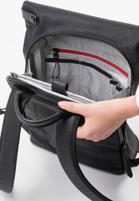 Zaino nero con chiusura a roll-top. L'interno presenta un motivo a griglia grigia, una tasca con zip rossa e vari scomparti per l'organizzazione. Texture in morbida pelle.