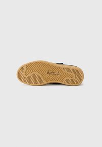 Svart sneakersula med ett strukturerat mönster av gummigummi. Har en framträdande Reebok-logotyp och en zigzag-däckdesign för grepp.