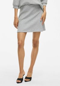 Mini-jupe de sport grise en tissu mélangé coton, présentant un design simple et ajusté, ainsi qu'une texture lisse. Associée à des talons ouverts noirs.