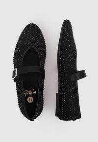 Black ballet flats with an upper covered in small spikes, round toe, and strap with a silver buckle. Smooth inner lining and flat sole.