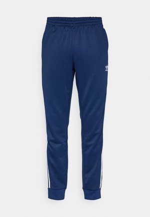 Navy blue Adidas track pants with elastic waistband, cuffed ankles, and white stripes down the sides, featuring small white Adidas logo on left thigh.