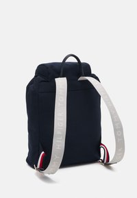 Mochila navy hecha de tela con una parte superior redondeada, que presenta correas grises con la marca "TOMMY HILFIGER" y acentos rojos y blancos a los lados.
