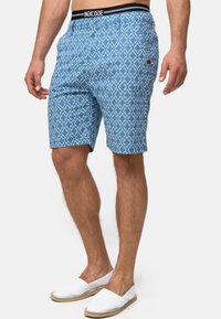 Shorts bleus à motif géométrique, confectionnés dans un tissu léger. Dotés d'une taille élastique et d'une poche latérale sur la droite.