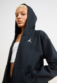 Sudadera con cremallera negra hecha de mezcla de algodón, con un logo Jumpman blanco en el lado izquierdo del pecho y capucha con cordones. Textura suave.