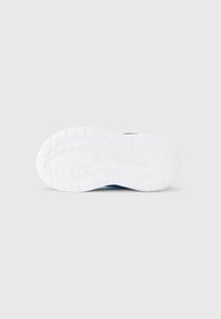 Podplat superge iz belega gumija z vzorcem teksturiranega prijema; modri poudarki so vidni na zgornjih straneh, z zaobljeno obliko in brezšivnim dizajnom.