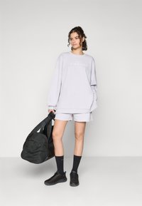 Sweat-shirt oversize gris clair avec le texte "ATHLEISURE", associé à un short assorti. Sac de sport noir et baskets, chaussettes noires à mi-mollet.