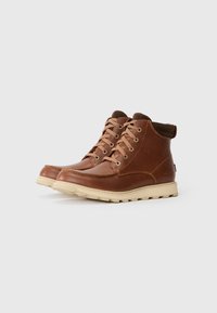 Botas marrones de cuero de media caña con un acabado suave, cordones beige y una suela de goma beige que presenta un patrón de relieve.