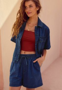 Jeansskjorta med korta ärmar, knäppning framtill och bröstfickor, tillsammans med en vinröd croptop och matchande denimshorts med dragsko.