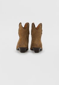 Bottes de cheville western en suède marron avec un bout pointu, des coutures courbées sur le dessus et un talon empilé. Doublure en cuir lisse et tirettes pour un enfilage facile.