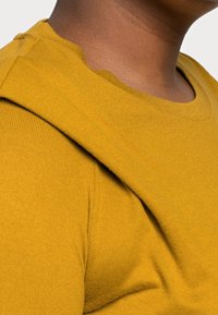 Chemise à manches courtes jaune moutarde avec une texture côtelée et un col rond. Présente un détail d'épaule superposé.