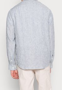 Chemise à manches longues rayée en coton bleu clair et blanc, avec un col classique, des poignets boutonnés et un ourlet légèrement courbé.