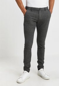 Graue, strukturierte Hose im Slim-Fit, mit flachem Bund, Gürtelschlaufen und Taschen, kombiniert mit weißen Sneakern.