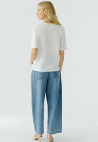 Witte top met korte mouwen in combinatie met lichtblauwe wijde jeans. De top heeft een ronde halslijn en de jeans hebben achterzakken en een losse pasvorm.