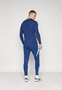 Maglietta atletica a maniche lunghe di colore blu navy abbinata a pantaloni coordinati con accenti blu chiaro e bande laterali, realizzati in tessuto elasticizzato leggero.