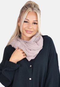 Écharpe rose clair texturée enroulée autour du cou, avec des bords effilochés, portée sur une chemise noire boutonnée. Le tissu semble doux et léger.