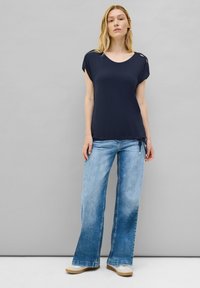 Haut bleu marine à manches courtes avec des détails découpés, associé à un jean flare bleu clair. Tissu doux, coupe décontractée et accents à cordon.