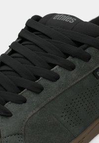 Γκρίζο σουέτ Sneakers με μαύρες κορδόνες, υφασμάτιες λεπτομέρειες και τρυπήματα στο πλάι. Ελαστική σόλα και διακριτική λεπτομέρεια branding στη γλώσσα.